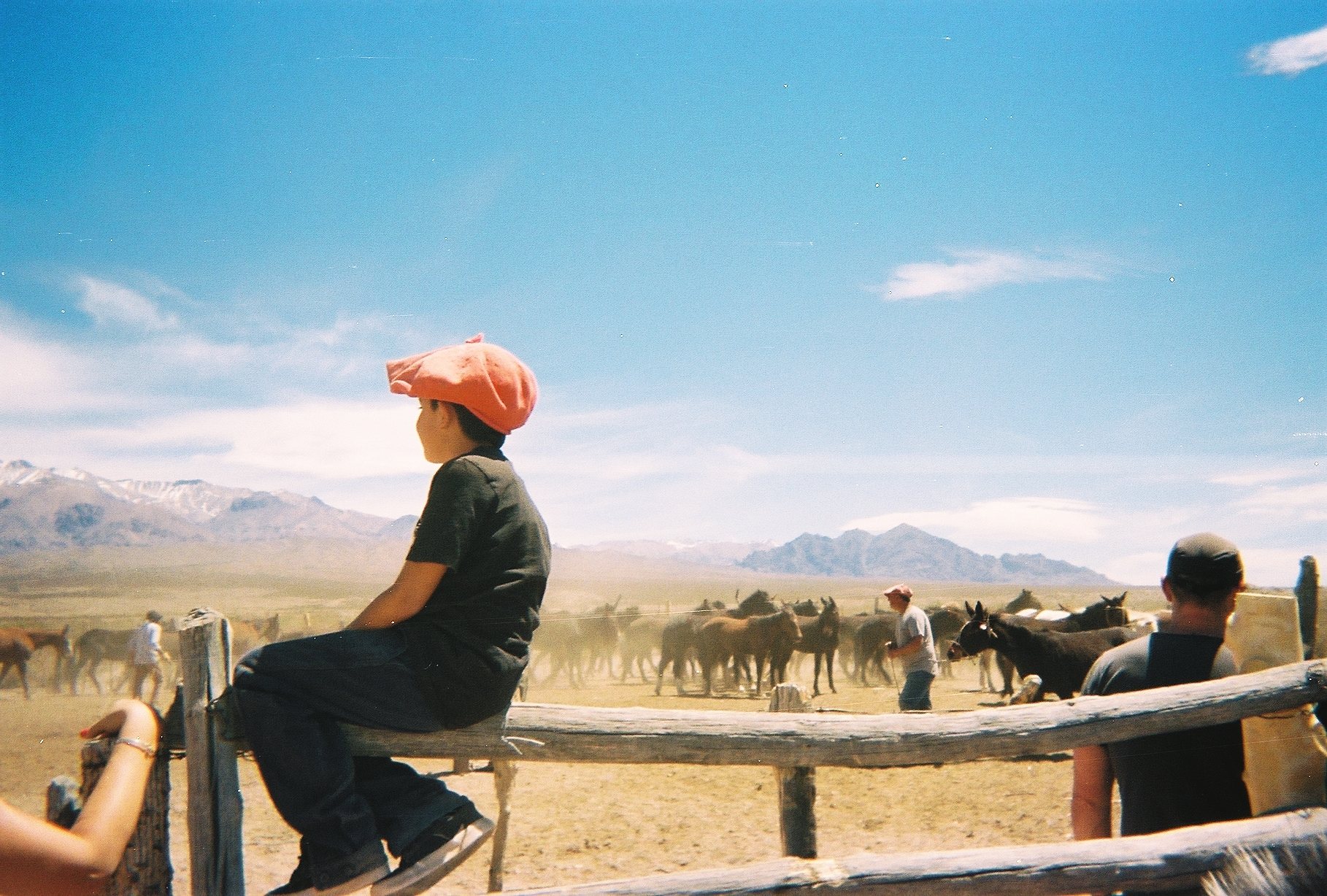 A boy in a red beret sitting on a corral fence