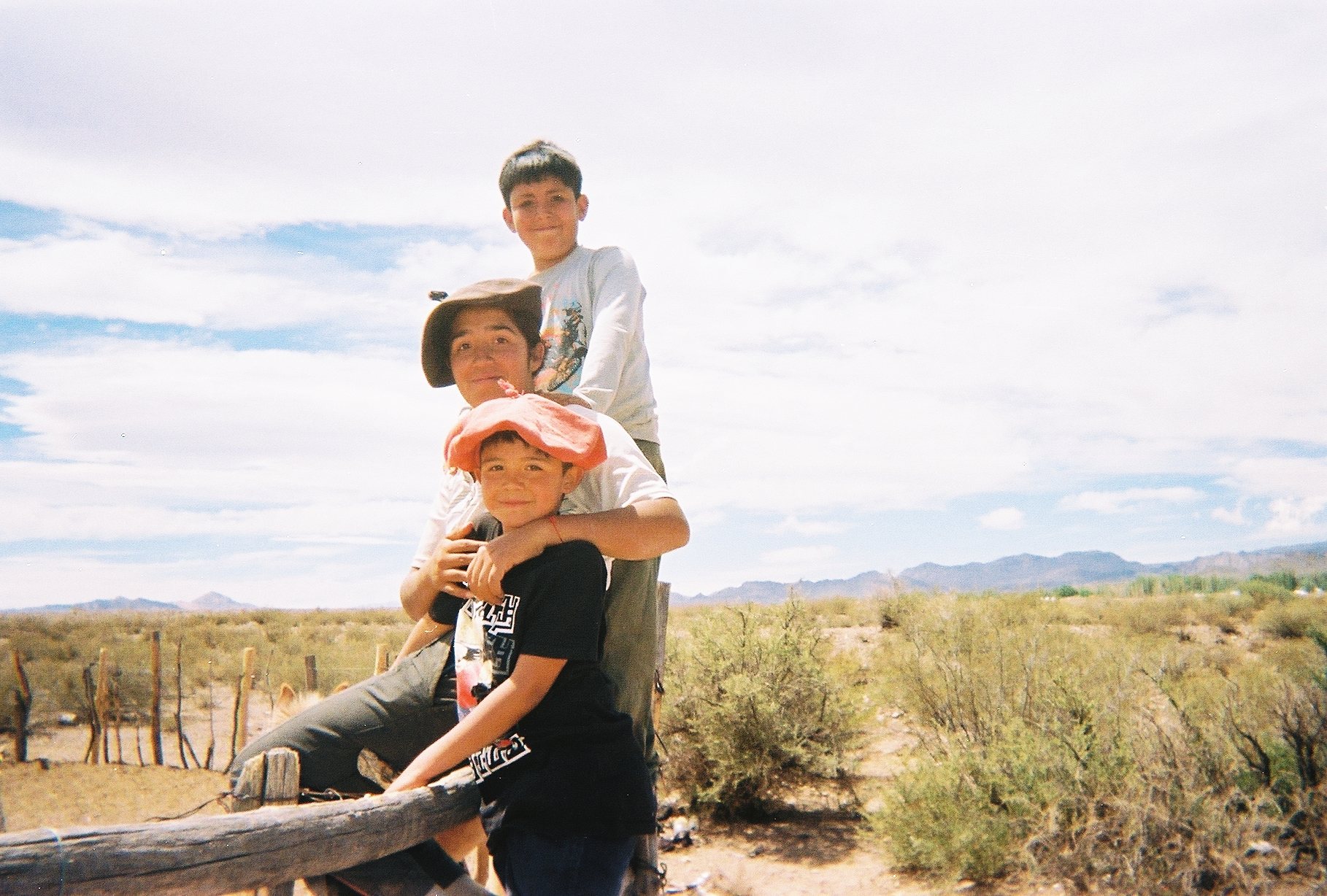 Three boys posing on a corral fence